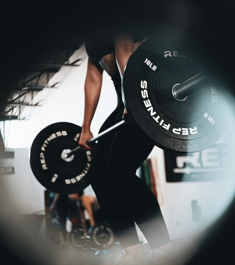 woman in black tank top and black leggings holding black barbell