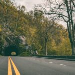 concrete road leading to a mountain tunnel covered in green trees during day